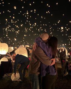 two people embracing each other in front of many lanterns flying above them at night time