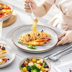 a woman is eating pasta with shrimp and broccoli on the table next to other dishes