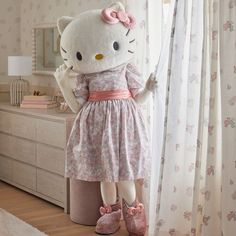 a hello kitty doll standing next to a window in a room with floral wallpaper