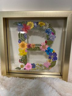 the letter e is made out of flowers and leaves in a gold frame on a white rug