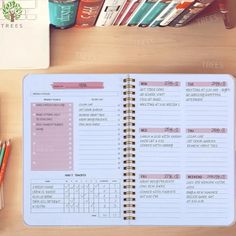 an open planner sitting on top of a wooden desk next to books and pencils