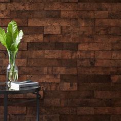 a glass vase with a green plant in it on a table next to a brick wall