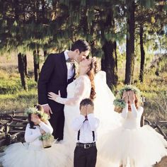 a bride and groom kissing in front of their children wearing tutu skirts with flower crowns