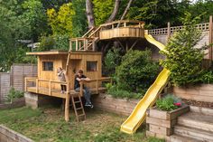 two children playing in a backyard with a slide and tree house on the other side