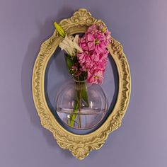 pink and white flowers in a glass vase on a mirror frame against a purple wall