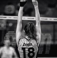 a female volleyball player is reaching up to hit the ball with her racket in black and white