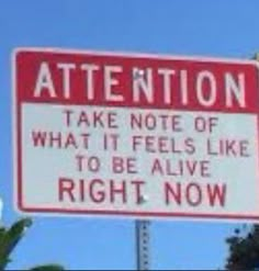 a red and white sign that says attention take note of what it feels like to be alive right now