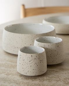 three white bowls sitting on top of a table next to each other with black speckles