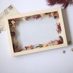 an empty wooden frame sitting on top of a white table next to some dried flowers