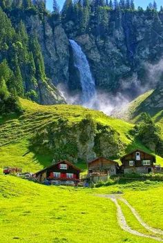 a green field with houses and a waterfall in the background