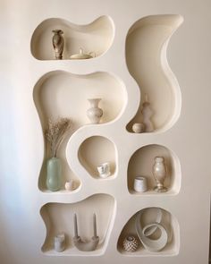 shelves with vases and other items on them in the shape of wavy shapes, arranged against a white wall