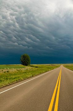 an empty road with yellow painted lines on the side and dark clouds in the background