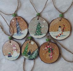 six ornaments are hanging from twine strings on a white surface with snowmen and christmas trees