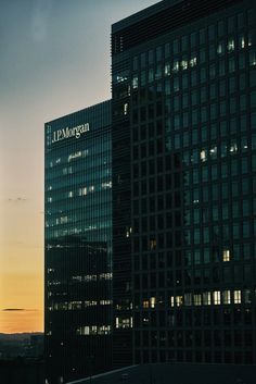 the sun is setting behind two skyscrapers with windows lit up in different colors and shapes