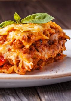 a white plate topped with lasagna covered in meat and cheese, garnished with basil