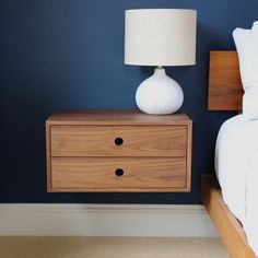 a white lamp sitting on top of a wooden dresser next to a bed