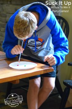 a young boy sitting at a table with a paper plate and toothbrush in his mouth