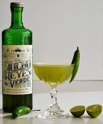 a bottle of alcohol next to a glass filled with green liquid and two limes