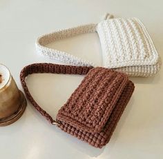 two crocheted purses sitting on top of a table next to a cup