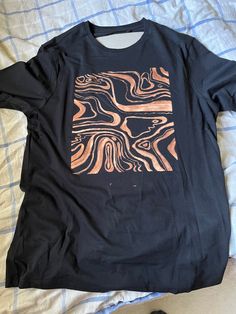 a black t - shirt with an orange and brown design on the front sitting on a bed