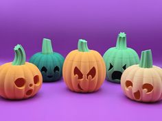 four pumpkins with faces carved into them on a purple surface, one is green and the other is orange