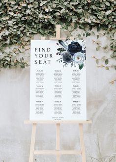 an easel stands in front of a wall with greenery and a seating chart