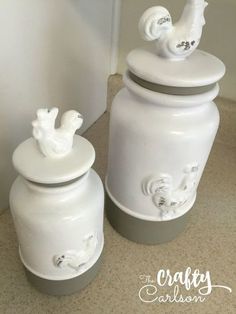 two white canisters sitting on the floor next to each other with rooster figurines