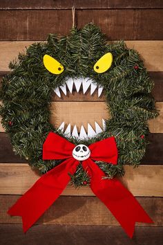 a wreath with a monster's mouth and red bow hanging on a wooden wall