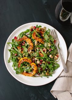 a white plate topped with salad next to a glass of wine and a silver fork