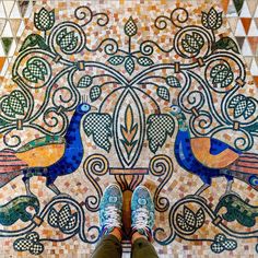 someone's feet standing in front of a colorful tile floor with birds on it