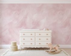 a baby's room with pink walls and white furniture, including a rocking horse