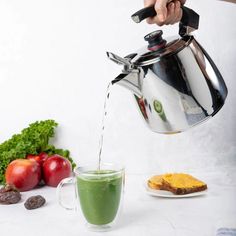 a person is pouring green tea into a glass cup next to some fruits and vegetables