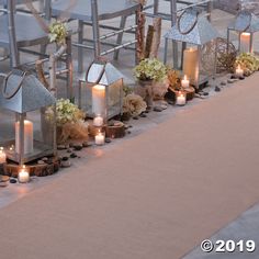 several lit candles are lined up on a long table with flowers and other decorative items