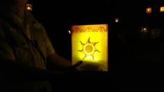 a person holding a lit up paper lantern with the sun on it in the dark