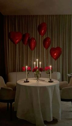 the table is set with candles and red heart balloons in the shape of hearts on it