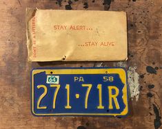 a blue and yellow license plate sitting on top of a piece of wood next to an envelope