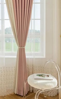 a chair and table in front of a window with pink drapes on the windowsill