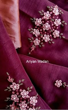 an embroidered purple fabric with pink flowers on the bottom and side, is shown in close up