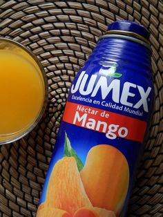 a can of mango juice next to a glass filled with orange juice on a wicker table