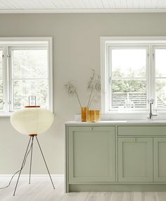 a kitchen with green cabinets and white counter tops next to two large windows on the wall