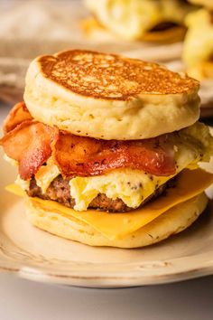 a bacon, egg and cheese breakfast sandwich is on a plate with pancakes in the background