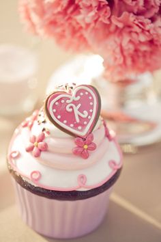 a pink cupcake with a heart on top next to a vase filled with flowers