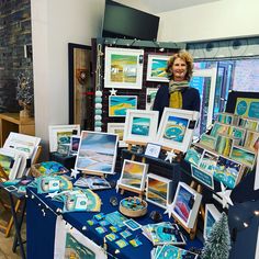 a woman standing next to a table with paintings on it