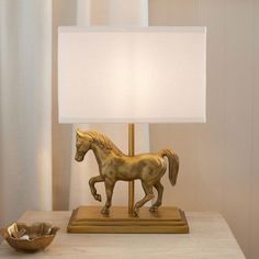 a horse figurine on a table next to a lamp with a white shade