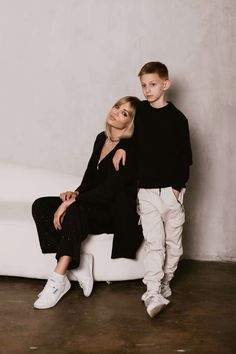 a woman sitting next to a boy on a white couch in front of a wall