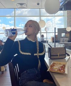 a woman sitting at a table drinking from a bottle