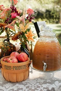 a wooden basket filled with apples sitting on top of a table next to a vase full of flowers