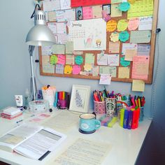 a white desk topped with lots of notes and papers next to a lamp on top of it