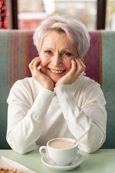 an older woman sitting at a table with a cup of coffee in front of her