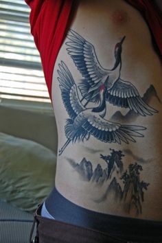 a woman with a tattoo on her stomach has two birds flying over the mountains and trees